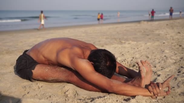 En man på stranden gör yoga på stranden mot bakgrund av havet — Stockvideo