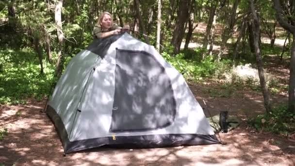 Giovane donna attraente installa una tenda sulla natura. Ragazza turista nella foresta — Video Stock