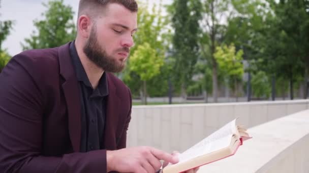 Un hombre de negocios está leyendo un libro en un parque. Un hombre lee un libro al aire libre — Vídeo de stock