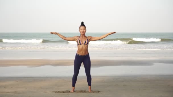 Доросла жінка робить йогу на пляжі на тлі моря — стокове відео