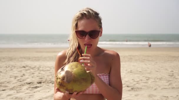 Piękna blondynka trzyma kokosa na tropikalnej plaży — Wideo stockowe