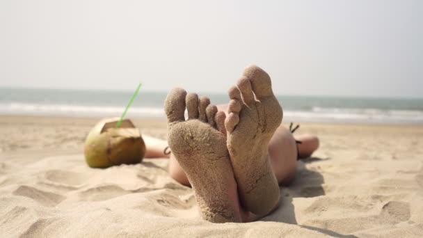 Een vrouw is ontspannen en zonnebaden op een tropisch zeestrand. Voeten in zand close-up — Stockvideo