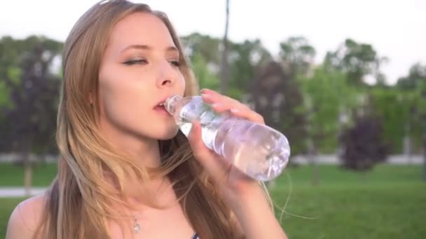 La giovane donna beve acqua da una bottiglia in un parco all'aperto. Ragazza beve acqua — Video Stock