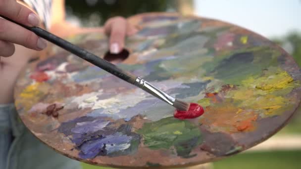 Mujer artista mezcla pintura en una paleta de madera y pinta un cuadro. Artista chica . — Vídeos de Stock