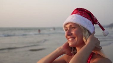 Gün batımında tropik bir plajda Noel şapkalı mutlu bir kadının portresi.