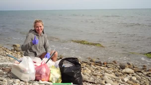 Donna ecologista con pacchetti di spazzatura sulla spiaggia mare mostra pollici in su — Video Stock