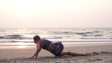 Sportif kız sahilde denizin arka planında antrenman yapıyor.