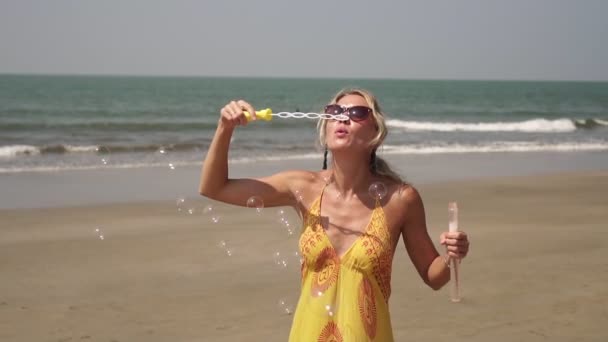 Uma jovem mulher em um vestido de verão brilhante está soprando bolhas. Menina com bolhas de sabão — Vídeo de Stock