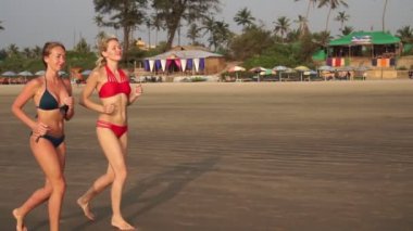 Bir çift güzel kız deniz kıyısında koşuyor, kumsalda, ağır çekimde
