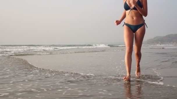 Jovem mulher bonita corre descalça ao longo das ondas do mar na praia arenosa — Vídeo de Stock