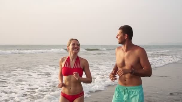 Fiatal szép pár férfi és nő kocog a tengerparton — Stock videók