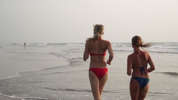 Красивые сексуальные женщины в купальниках бегают по морским волнам на пляже — стоковое видео