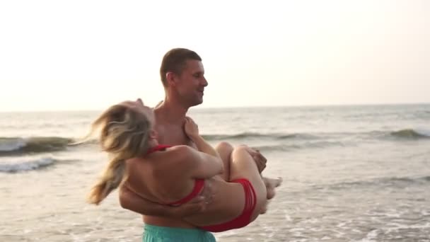 Geliefden, pasgehuwden, een man houdt een vrouw in zijn armen tegen de achtergrond van de zee — Stockvideo