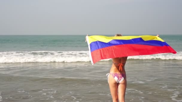 Mooie vrouw met de vlag van Colombia op de achtergrond van de zee. — Stockvideo