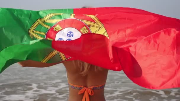 Mooie vrouw in een badpak met vlag van portugal op de achtergrond van de zee — Stockvideo