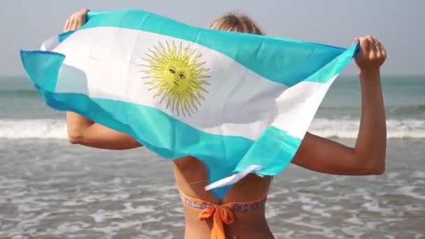 Schöne Frau mit der Flagge Argentiniens auf dem Hintergrund des Meeres. — Stockvideo