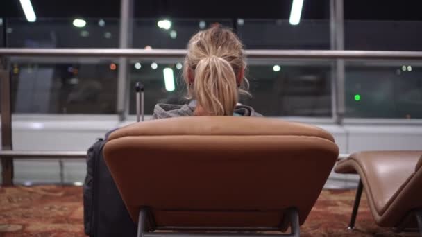 A female tourist is sitting in a chair in an airport or train station terminal — Stock Video