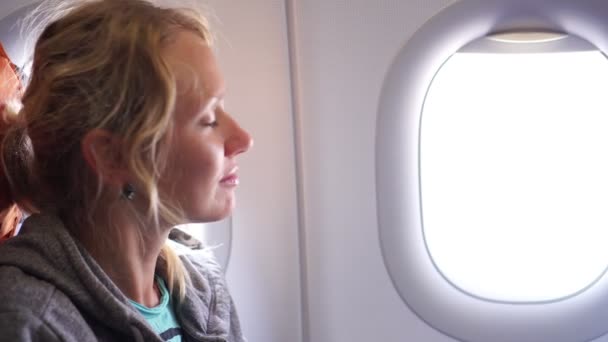 Спокойная женщина пассажир летает в самолете рядом с окном — стоковое видео