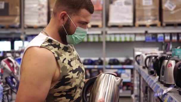 Retrato de un hombre con una máscara de protección médica en una tienda de electrodomésticos — Vídeos de Stock