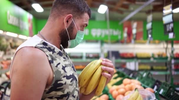 Tıbbi koruyucu maske takan erkek alışverişçi marketten ürün seçer — Stok video