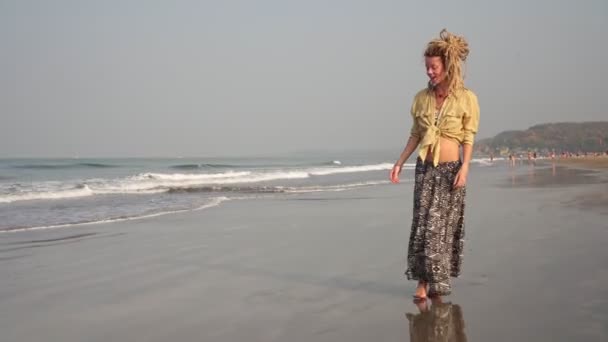 Una giovane donna in abito etnico cammina lungo la spiaggia di mare. Ragazza con capelli dreadlocks. — Video Stock