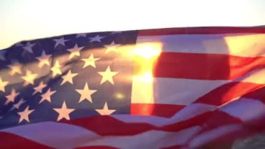 Sahilde günbatımının arka planında Amerikan bayrağı olan bir kadın. Amerikan bayrağı taşıyan kız.