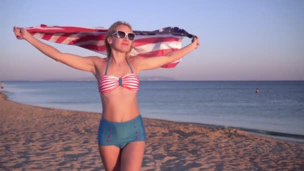 Красивая женщина на морском пляже с флагом США. Девушка в купальнике с американским флагом — стоковое видео