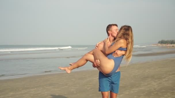 Romantyczna zakochana para, mężczyzna niesie kobietę w ramionach na tle morza. — Wideo stockowe