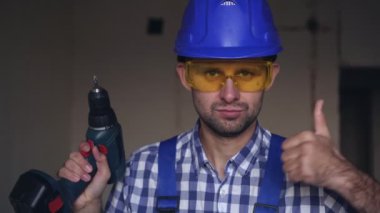 Elektrikli tornavidayla çalışan ciddi bir inşaat işçisi baş parmağını kaldırdı.
