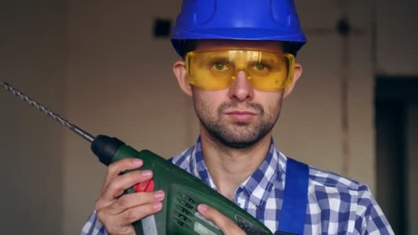 Retrato de un joven constructor o trabajador moderno con casco, gafas y una herramienta de construcción — Vídeo de stock