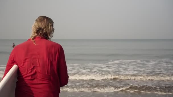 Un homme âgé aux cheveux gris va faire du sport et du surf. Un vieil homme avec une planche de surf va à la mer — Video