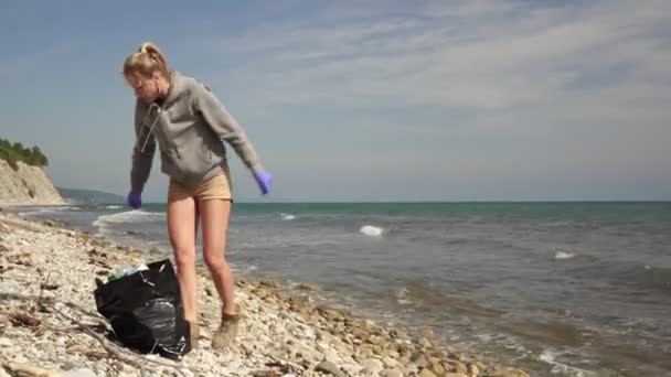 Young woman volunteer ecologist cleans the sea beach from garbage and plastic waste — Stock Video