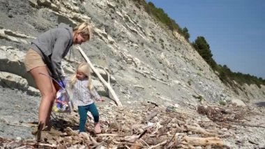 Çocuklu bir aile, deniz kıyısını çöpten temizler. Bir kadın ve bir kız plajda plastik temizliyorlar. Çevreciler ve gönüllüler çöpleri temizler