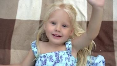 Küçük kız battaniyeye uzanır, elini sallar ve merhaba der.