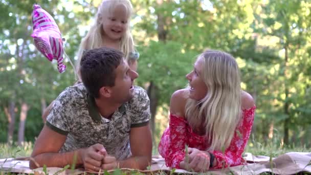 Gelukkig gezin met een kind in het park buiten. Mam, pap en het kind ontspannen op een deken in de natuur. — Stockvideo