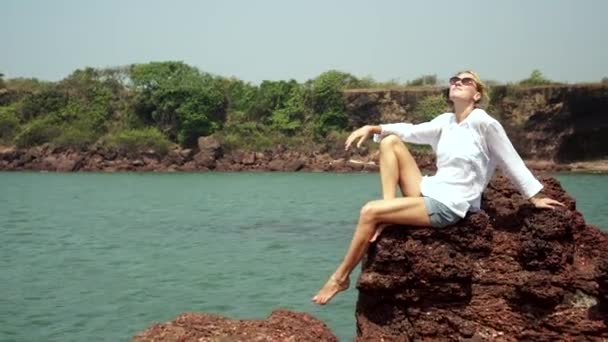 Mladá žena turista sedí na skále na pozadí moře — Stock video