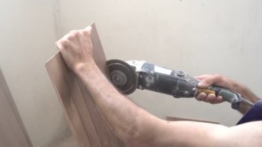 Bir erkek işçi, seramik bir fayansı öğütücüyle onarıp testereyle keser.