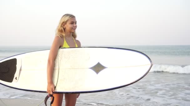 Jonge aantrekkelijke vrouw surfer staat met een surfplank op de achtergrond van de zee — Stockvideo
