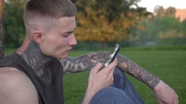 Een jonge crimineel met een smartphone. Bandiet of hooligan met tatoeages, straatcriminaliteit — Stockvideo