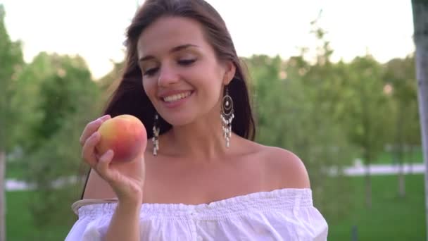 Attractive young woman with peach fruit outdoors. Woman is eating a ripe peach — Stock Video