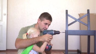 Baba ve kız mobilya montajı yapıyorlar. Bir çocuk ve babası elektrikli tornavidayla ahşap mobilyaları tamir ediyor.