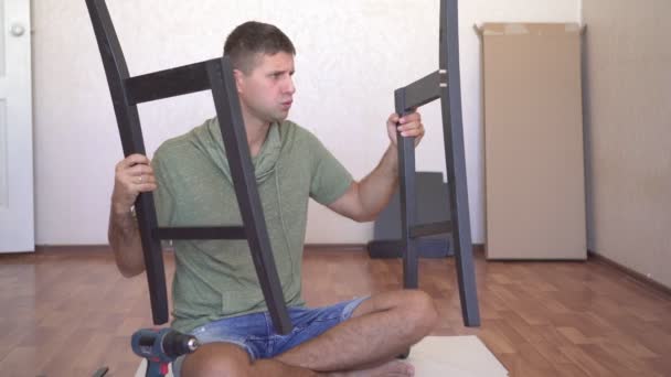 De ongelukkige man is meubels aan het monteren. De man weet niet hoe hij de meubels moet monteren. — Stockvideo