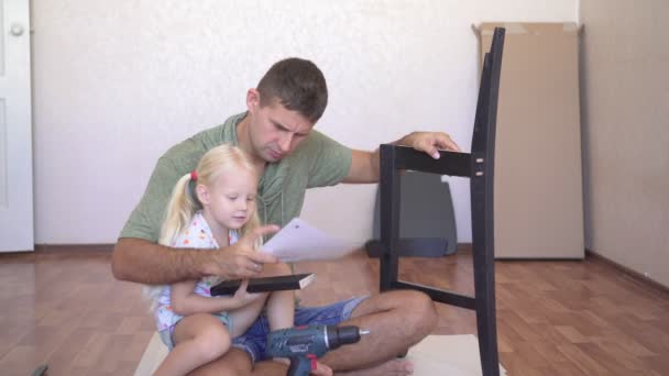 Папа и его дочь собирают мебель. Отец учит ребенка собирать мебель.. — стоковое видео
