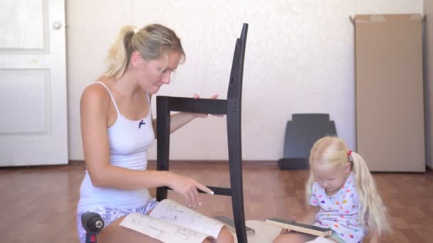Máma a dcera se snaží sestavit nábytek. Žena a dítě skládají dřevěný nábytek v novém domově. — Stock video