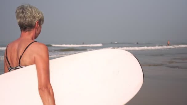 Maturo donna anziana attiva entra per lo sport e passeggiate sulla spiaggia con una tavola da surf — Video Stock