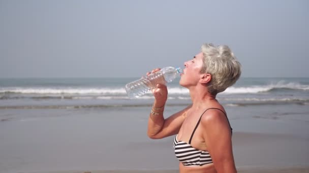 Atractiva pensionista madura bebe agua limpia de una botella sobre el fondo del mar — Vídeos de Stock