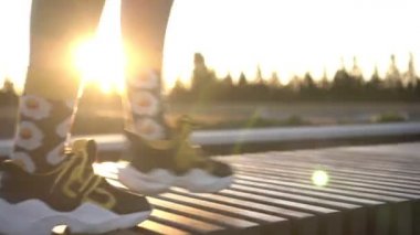Spor ayakkabılı bir kadın gün batımında arka planda yürür. Kadınların ayakları spor ayakkabılarla yürür.