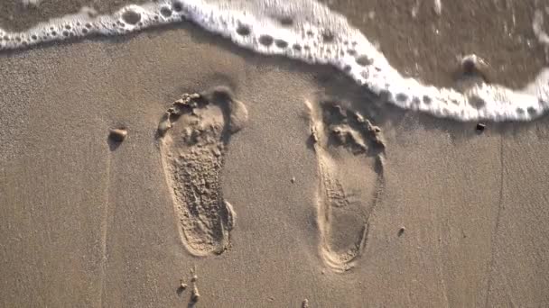 Menschliche Fußabdrücke im Sand und in der Meereswelle. Fußabdrücke eines Mannes am Strand — Stockvideo