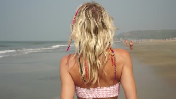 Attraente donna bionda in costume da bagno cammina lungo la spiaggia sullo sfondo del mare — Video Stock
