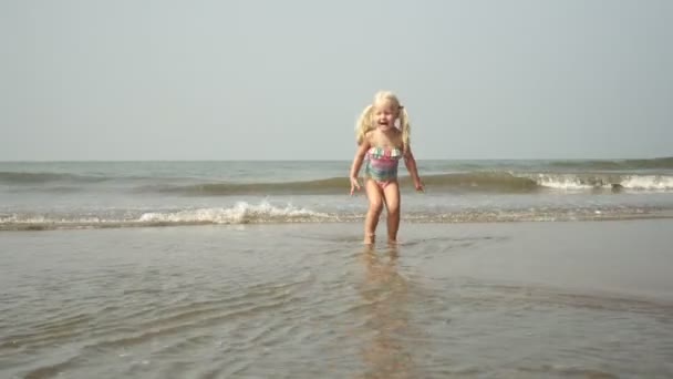Маленька дівчинка грає в хвилях на березі моря. Дитина плаває в морі в мілководді — стокове відео